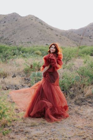 Elegant red gown with ruffled details flows gracefully in desert setting with mountain backdrop.