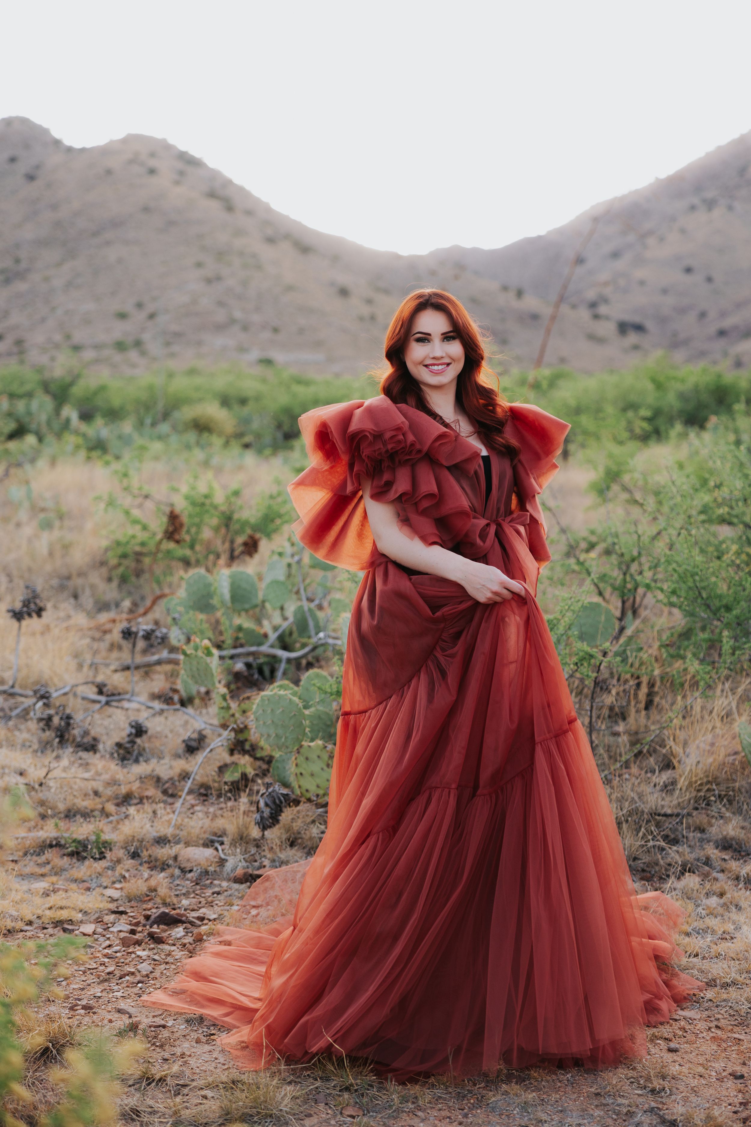 A dramatic red tulle dress creates movement and flow against a desert mountain backdrop.