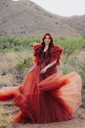 A flowing red tulle dress creates dramatic movement against rugged desert terrain.