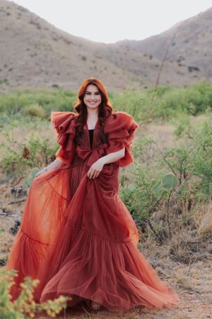 A romantic burgundy gown with flowing layers photographed against desert mountains.