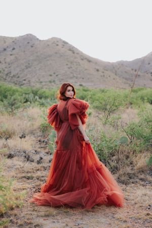 Dramatic red tulle dress creates ethereal movement against rugged desert terrain and mountains.