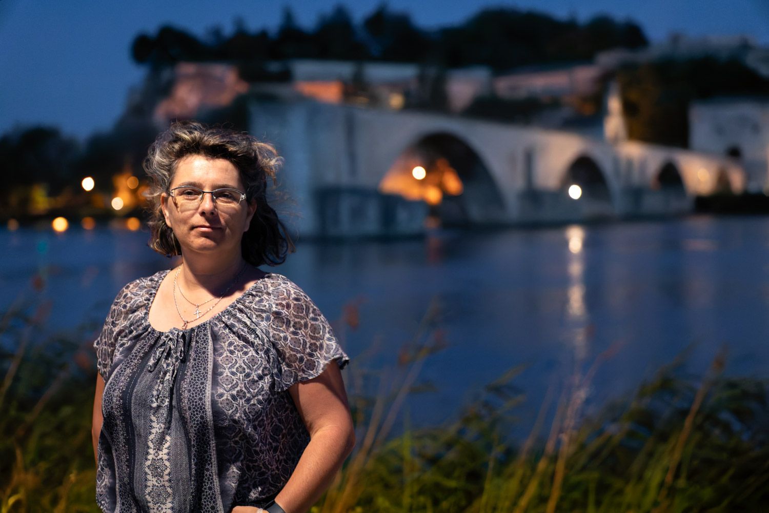 A twilight portrait by a waterfront with arched bridges and city lights in the background.