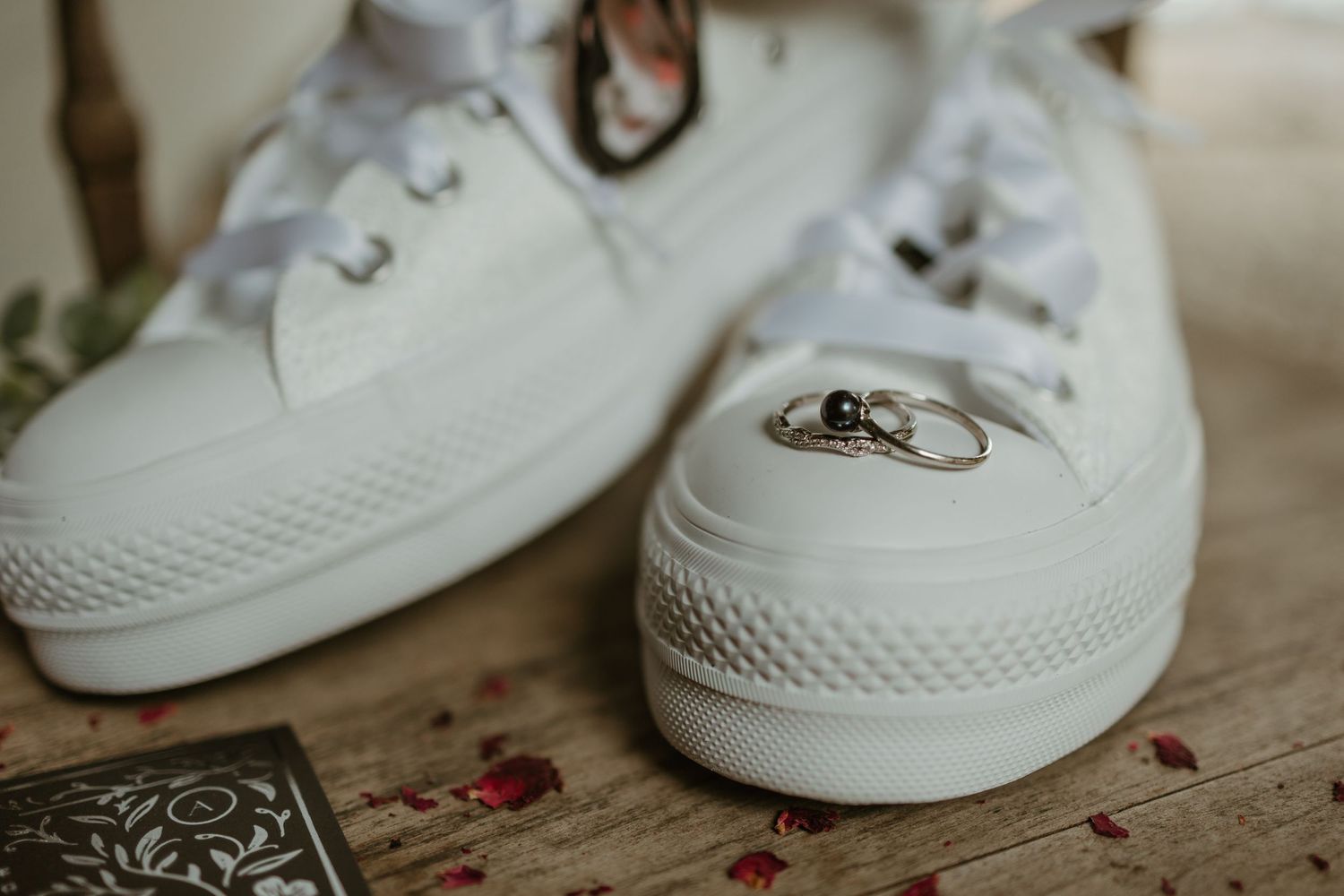 White sneakers with wedding rings balanced on the laces in an artistic detail shot.