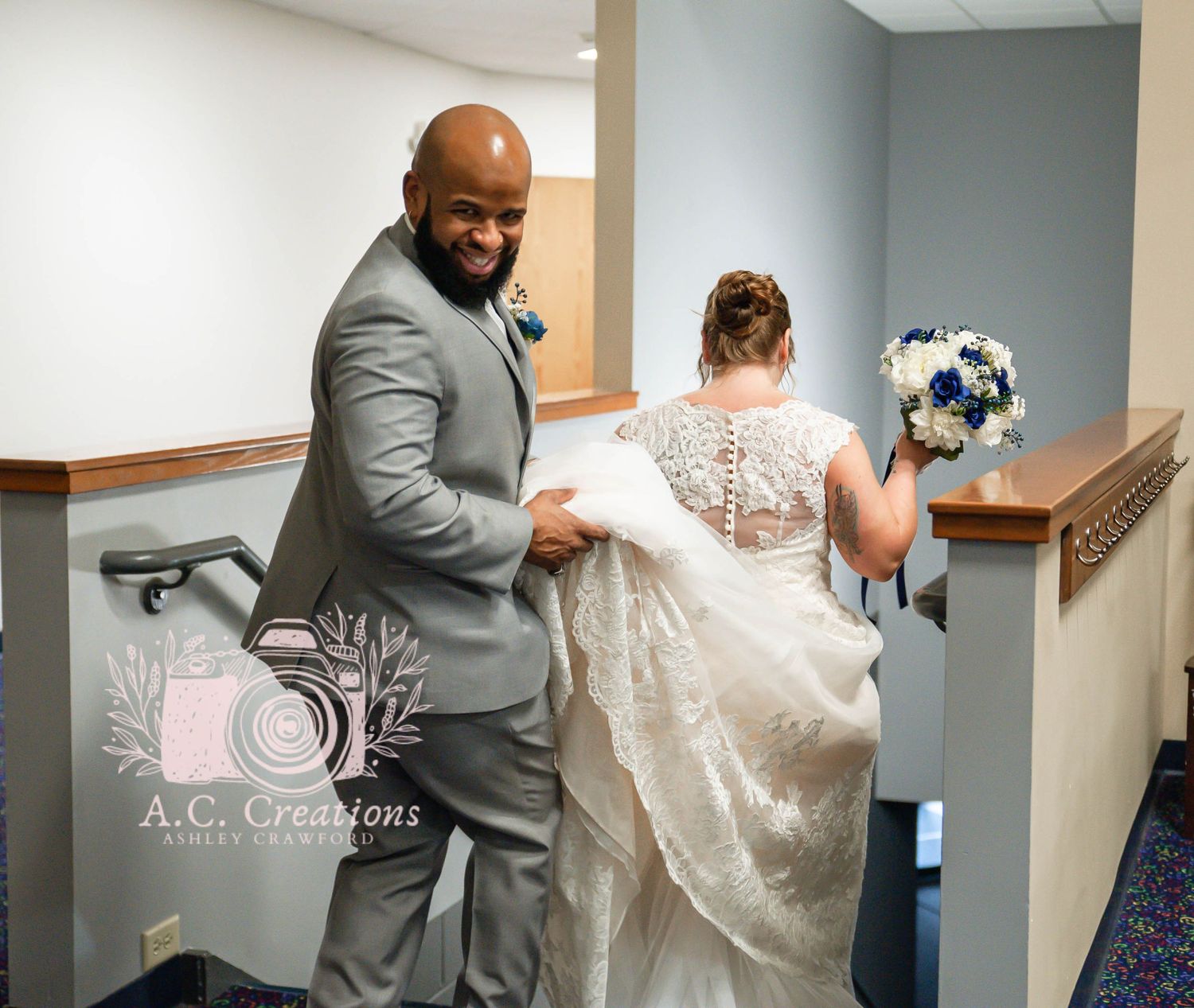 A couple in wedding attire share a playful moment in a hallway, with the groom assisting with the bride's dress.