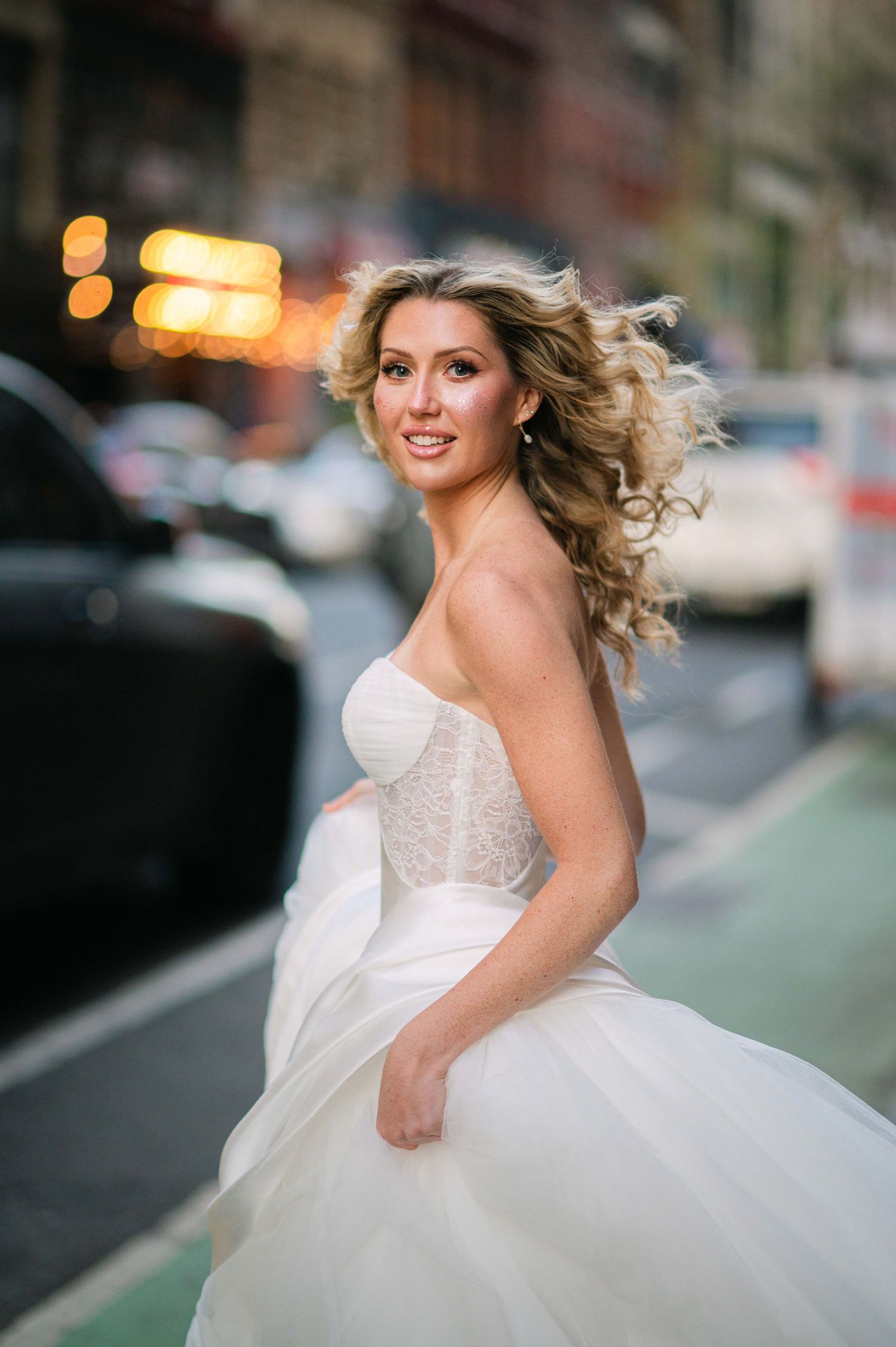 A bride in a flowing white tulle gown poses on a city street with windblown hair at golden hour. Hailey Paige