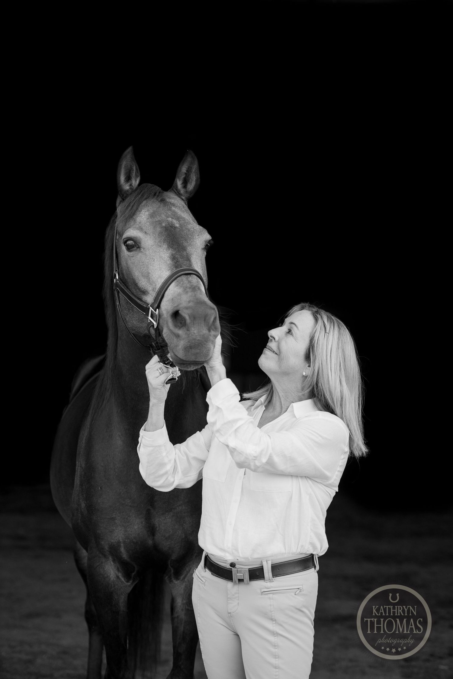 Black and white portrait of a horse and rider sharing an intimate moment against dark background.