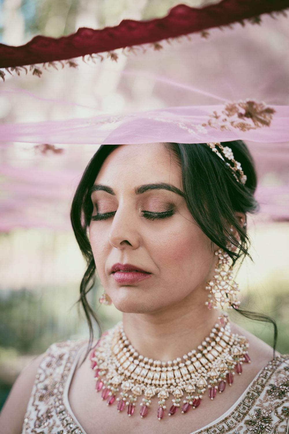 Close-up of intricate bridal jewelry and makeup with pearl necklace and pink details.