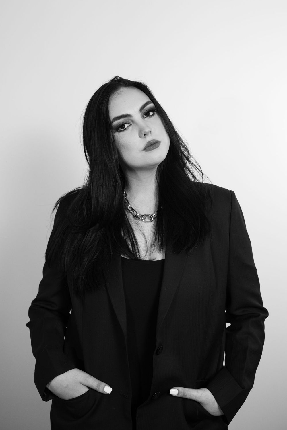Professional black and white portrait of someone in a black blazer and dark lipstick against a light background.