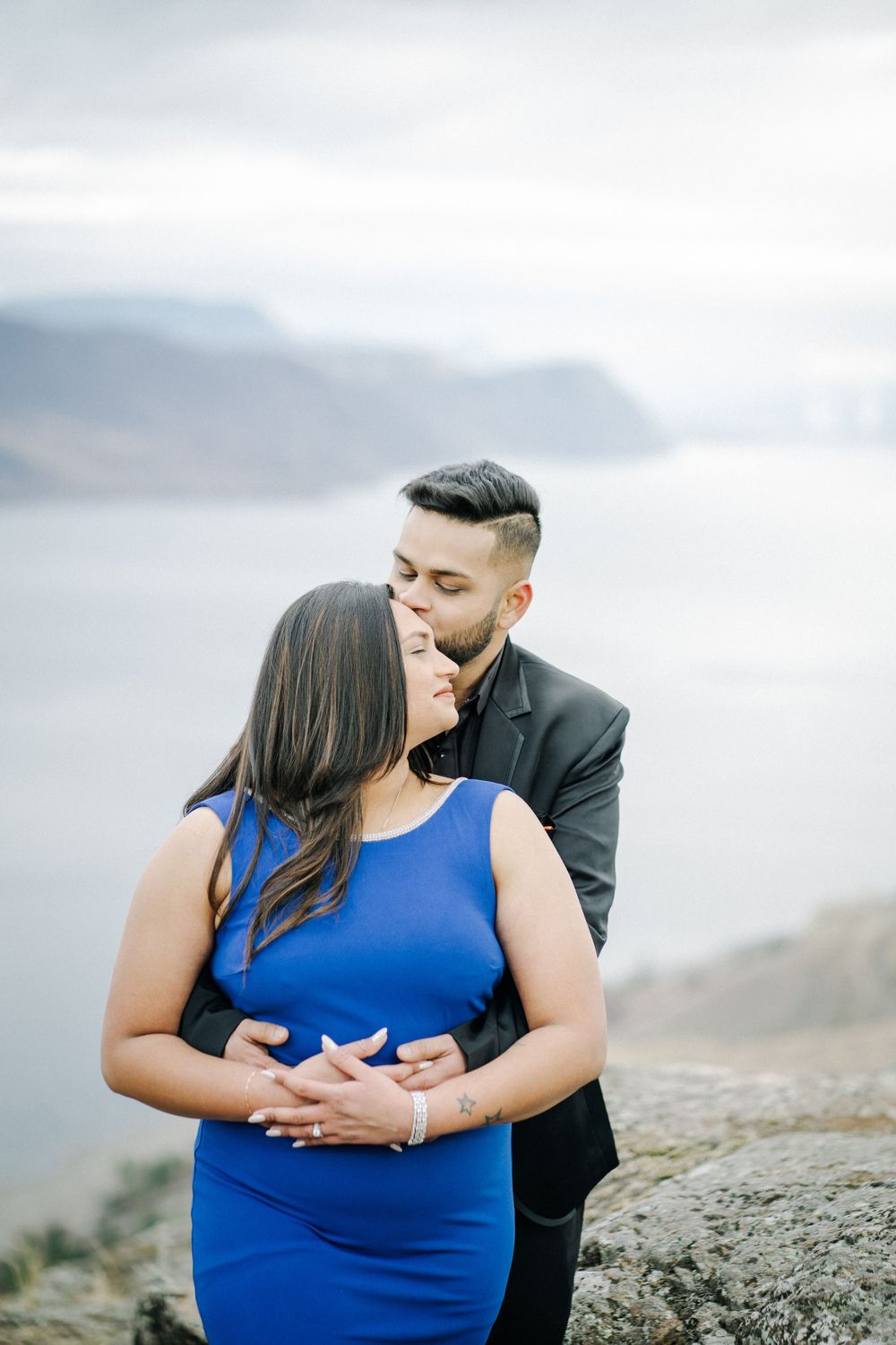 Intimate moment between couple on mountain overlook with dramatic cloudy background.