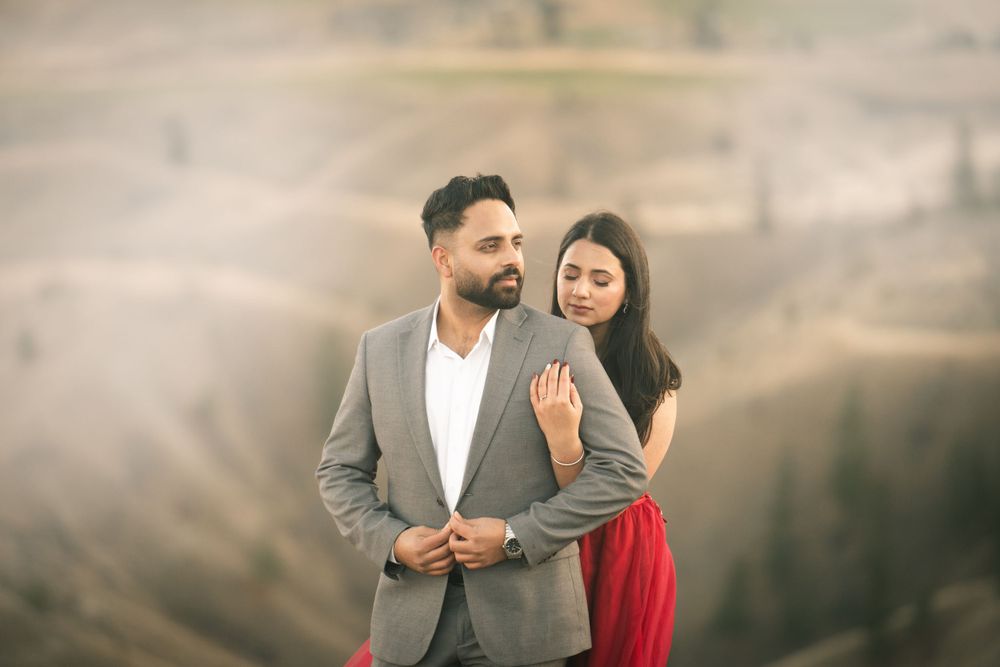 Stylish couple poses against mountain backdrop in grey suit and red dress.