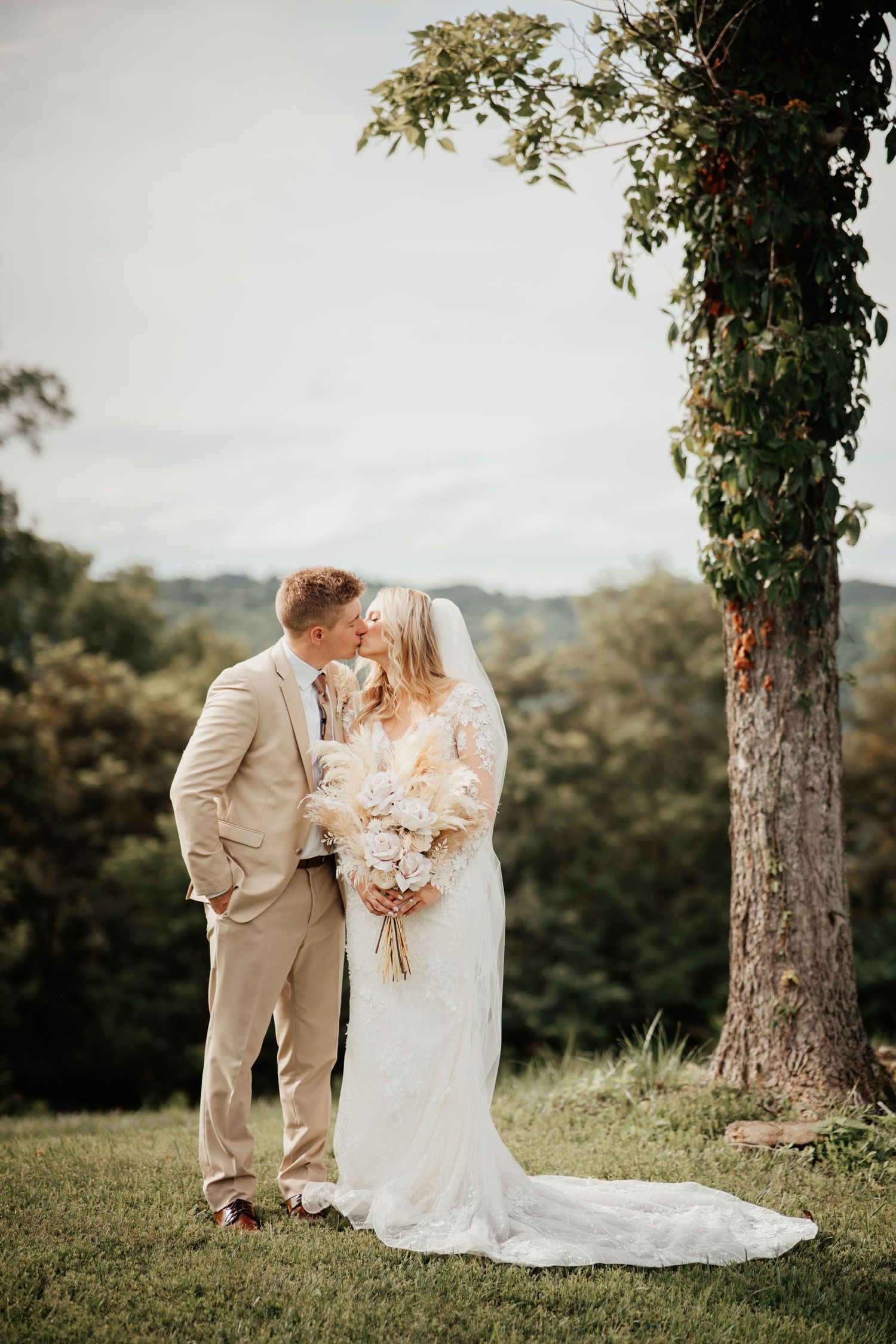 A romantic wedding couple shares an intimate moment under a tree in a scenic outdoor setting.
