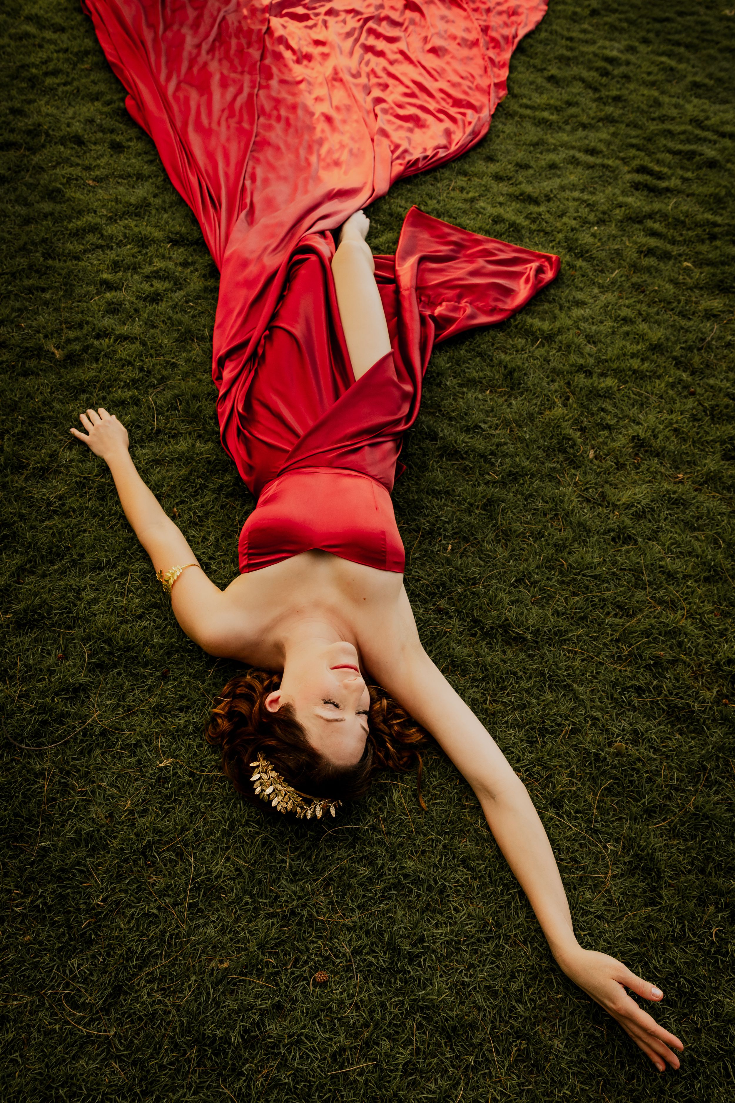 A flowing red dress spreads across green grass in an artistic pose.
