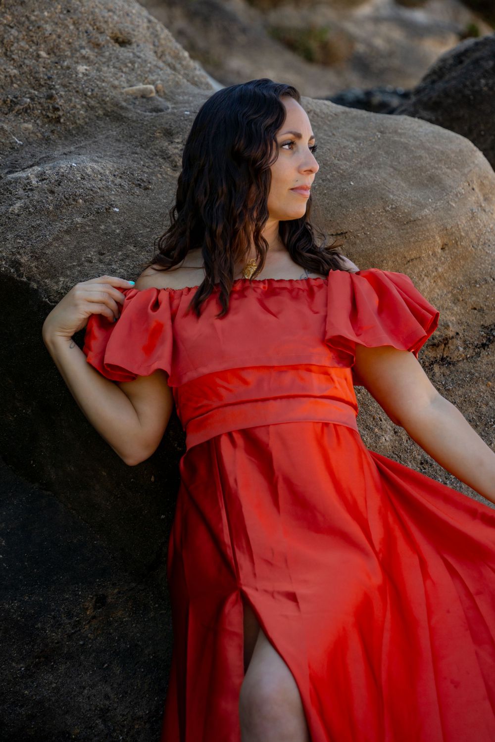 A ruffled red dress catches light against rocky coastal backgrounds.