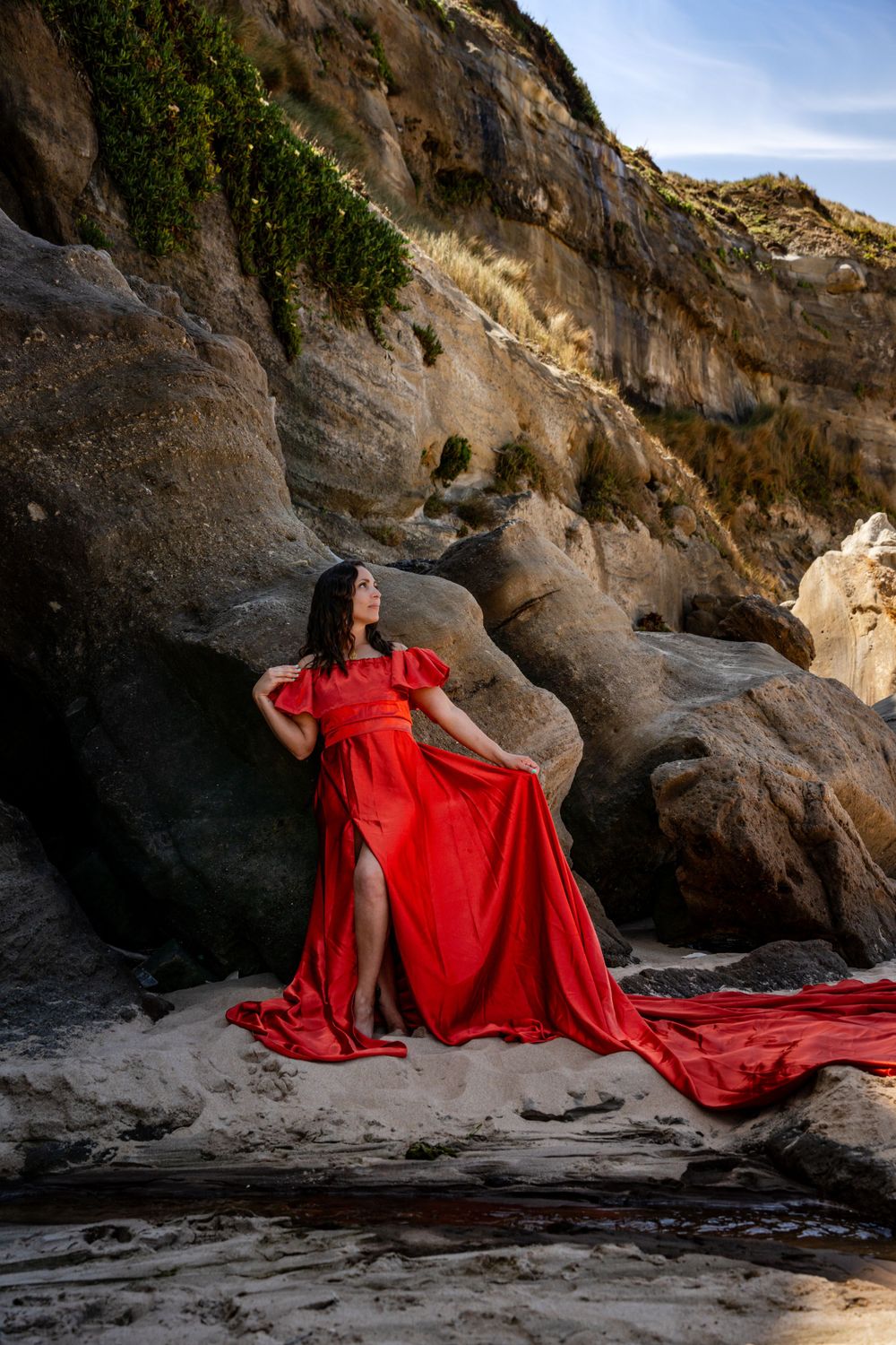 A red gown creates dramatic contrast against rocky cave formations at the beach.