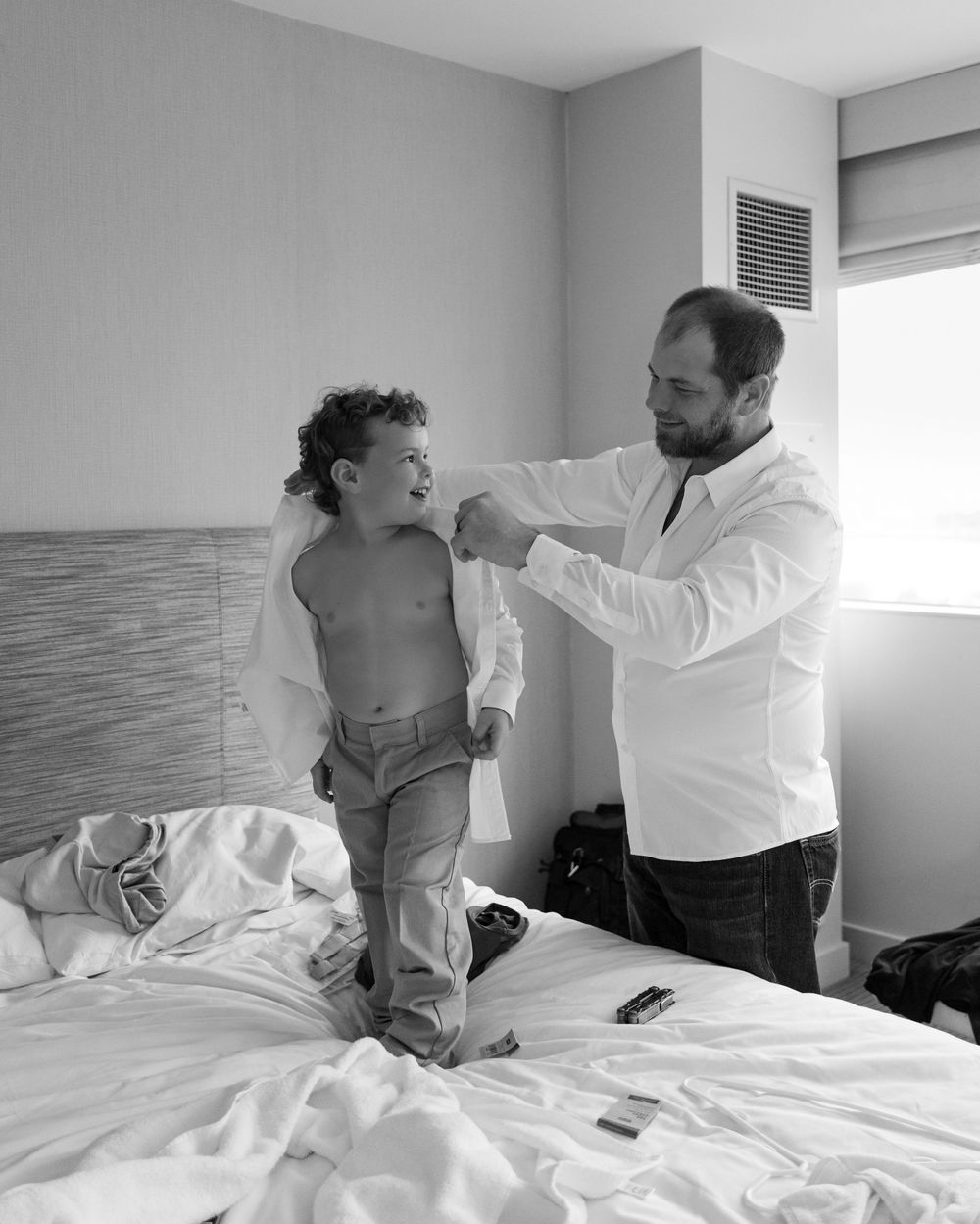 A series of black and white photos showing a parent helping a child get dressed in a bright bedroom setting.