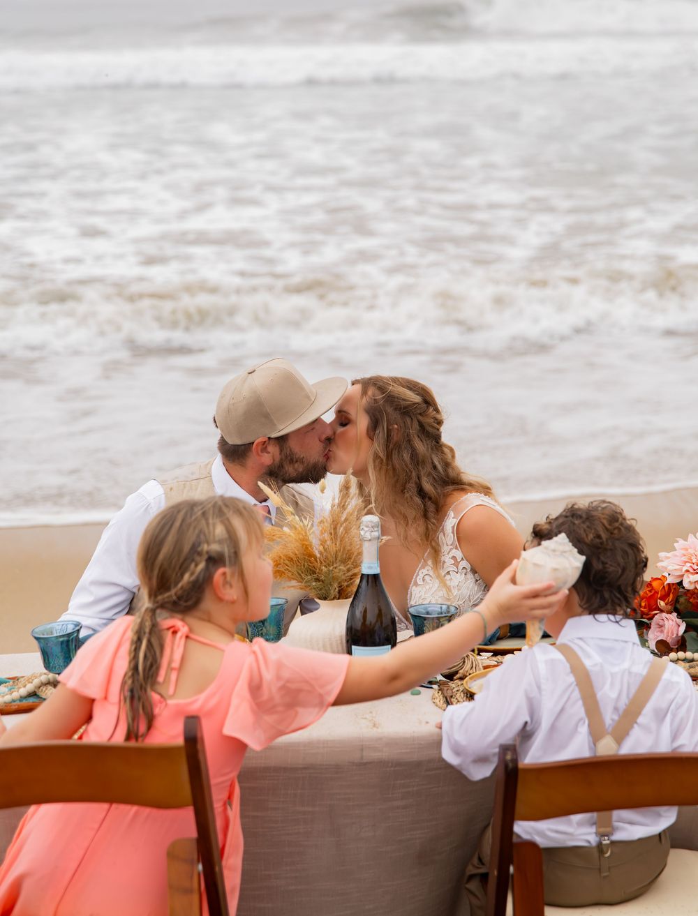 Group of people sitting together on a brown bench at the beach with waves visible in the background.