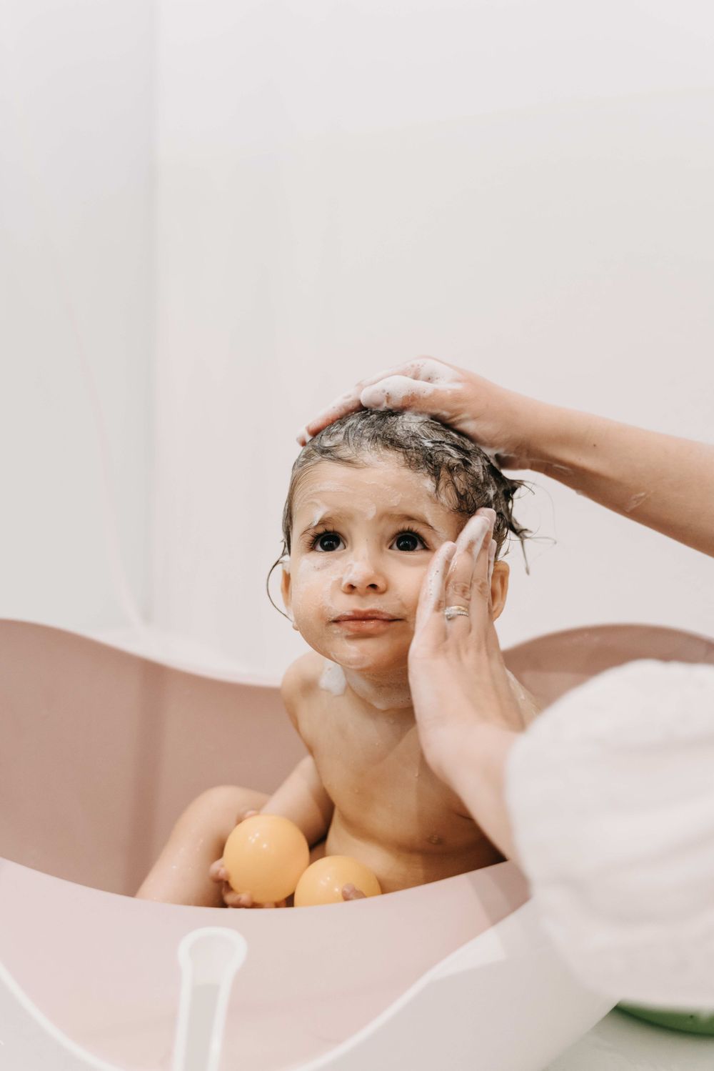 Gentle hands washing a small child during bath time with yellow rubber ducks floating nearby.