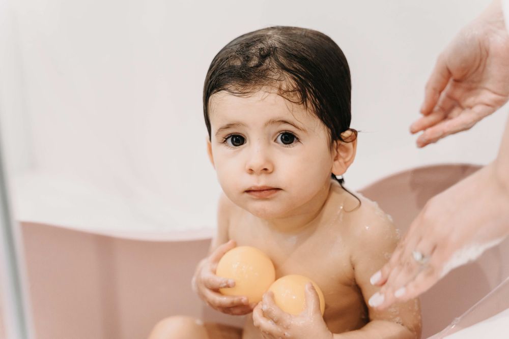 A bath time scene with small hands holding yellow rubber ducks in a pink tub.