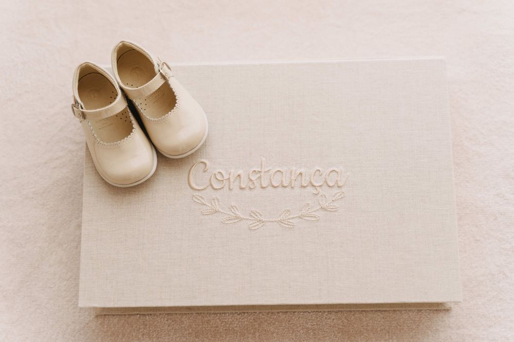 Elegant cream-colored baby shoes placed on an embossed christening invitation box.