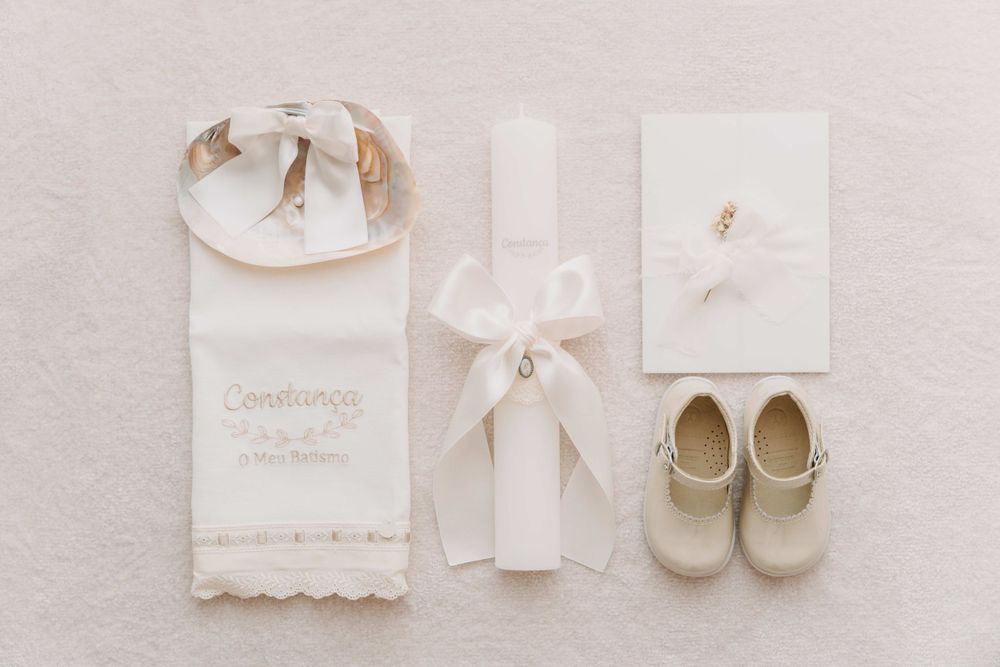 White christening accessories including a bib, bow, invitation and cream colored baby shoes on light fabric.