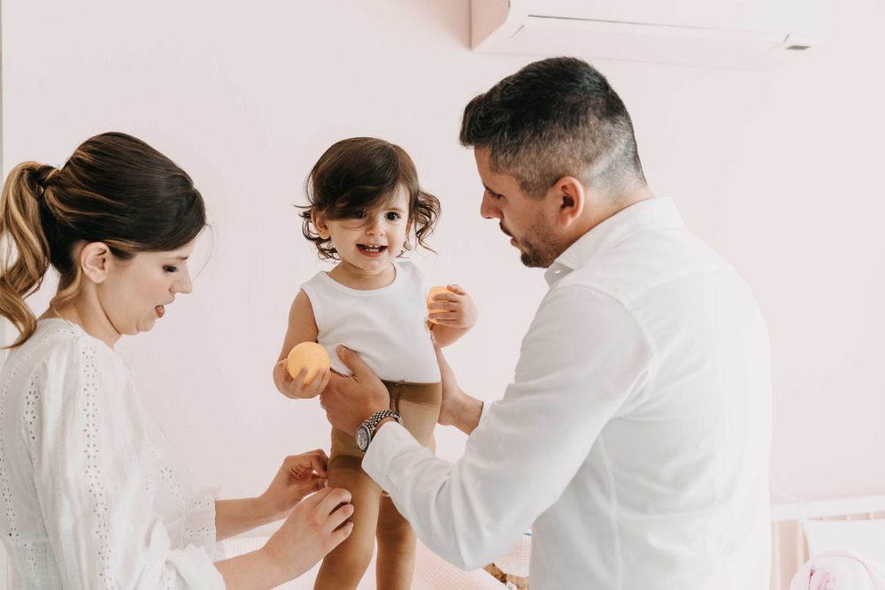 A heartwarming family scene with a toddler being dressed in white attire.