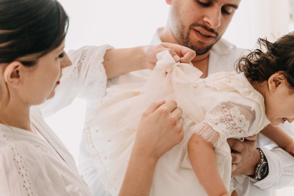 A tender family moment during a dress preparation in a bright white setting.