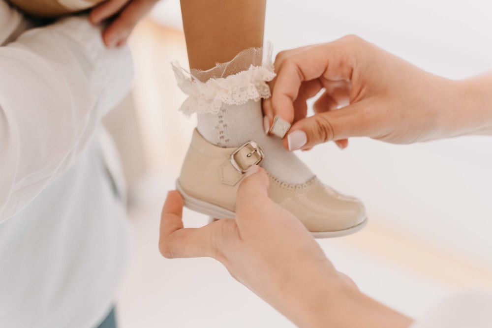 Close-up of hands fastening delicate lace on a beige shoe.