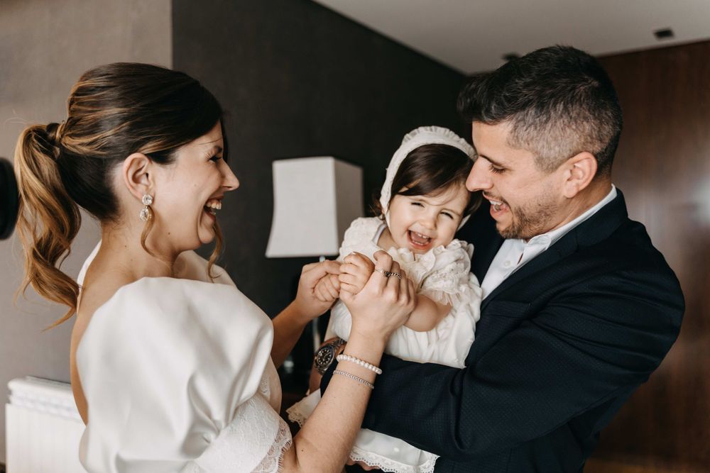A tender family moment with a baby in white being held and laughed with indoors.