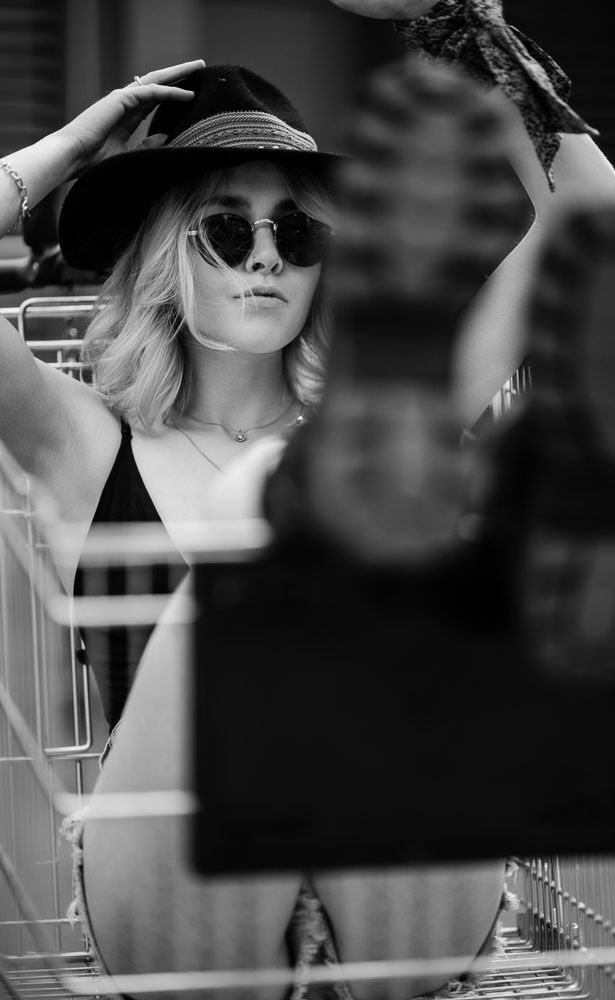Black and white photo of blonde woman in hat and sunglasses inside shopping cart.