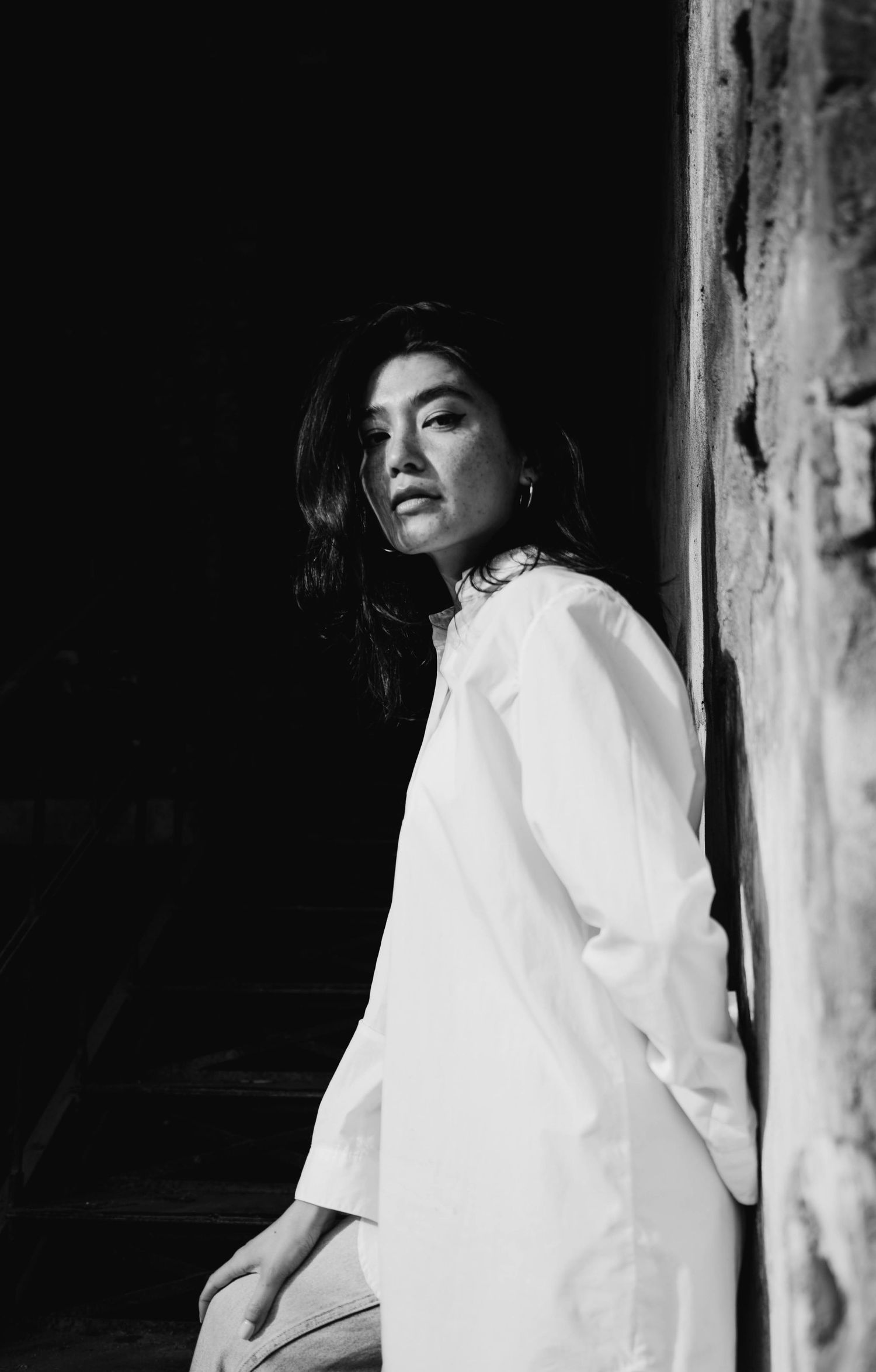 Black and white portrait of a woman wearing a white oversize shirt by the brick wall