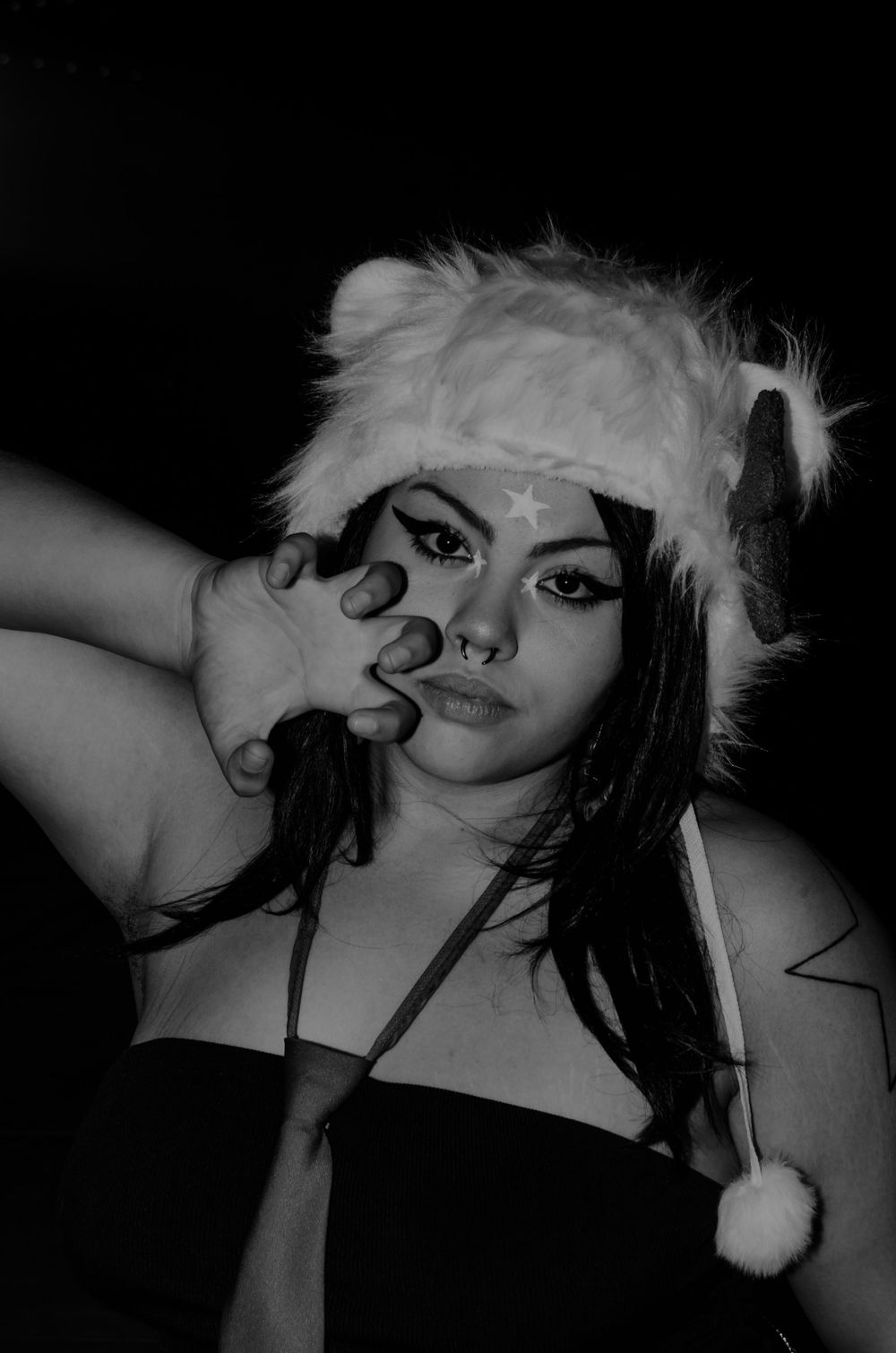 Artistic black and white portrait of someone in a festive white furry hat making dramatic pose.