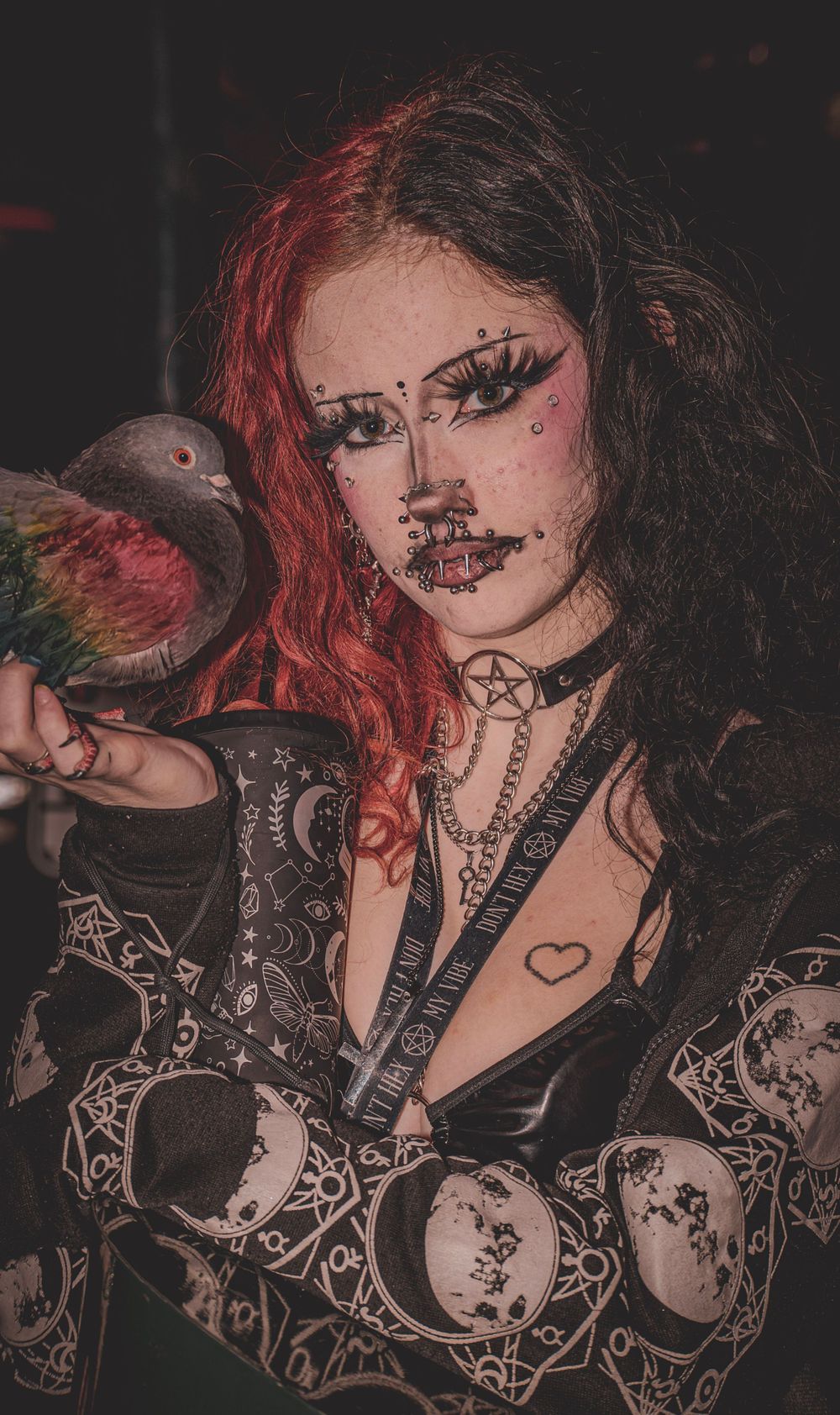 Gothic style portrait with dark makeup and red hair against black background.