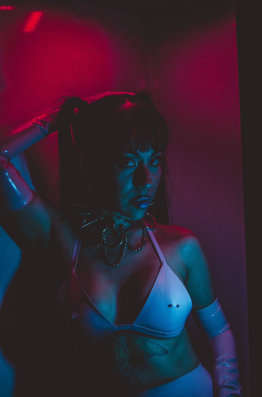 Dramatic portrait with red and blue lighting of person posing in dark setting.