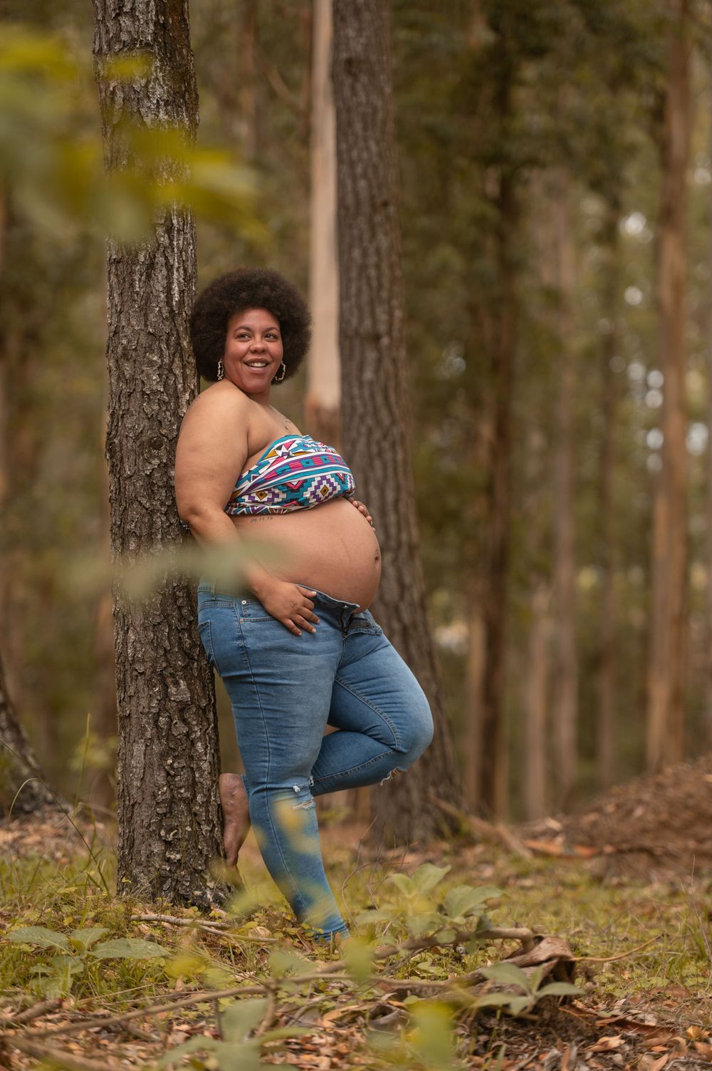 a pregnant woman standing leaning on a tree in the forest