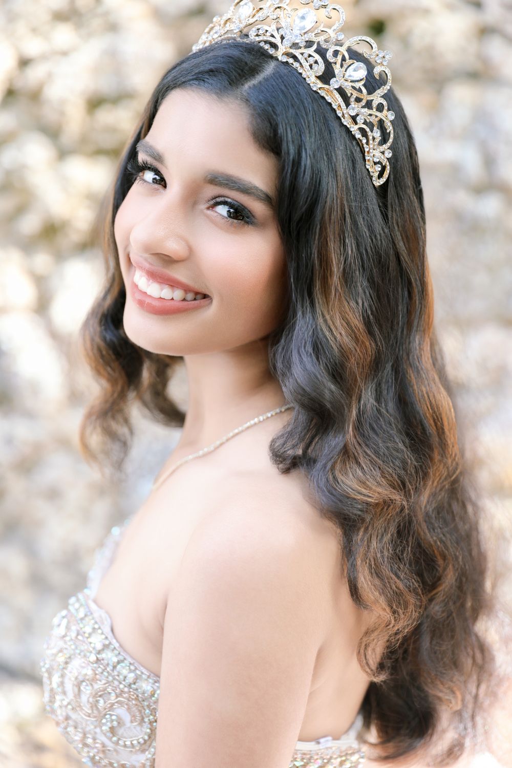 Crystal tiara and beaded gown detail shot against textured stone background.