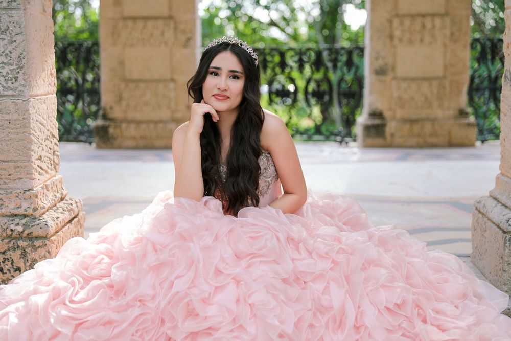 A quinceañera portrait session showcasing a voluminous pink ball gown in a columned outdoor setting.