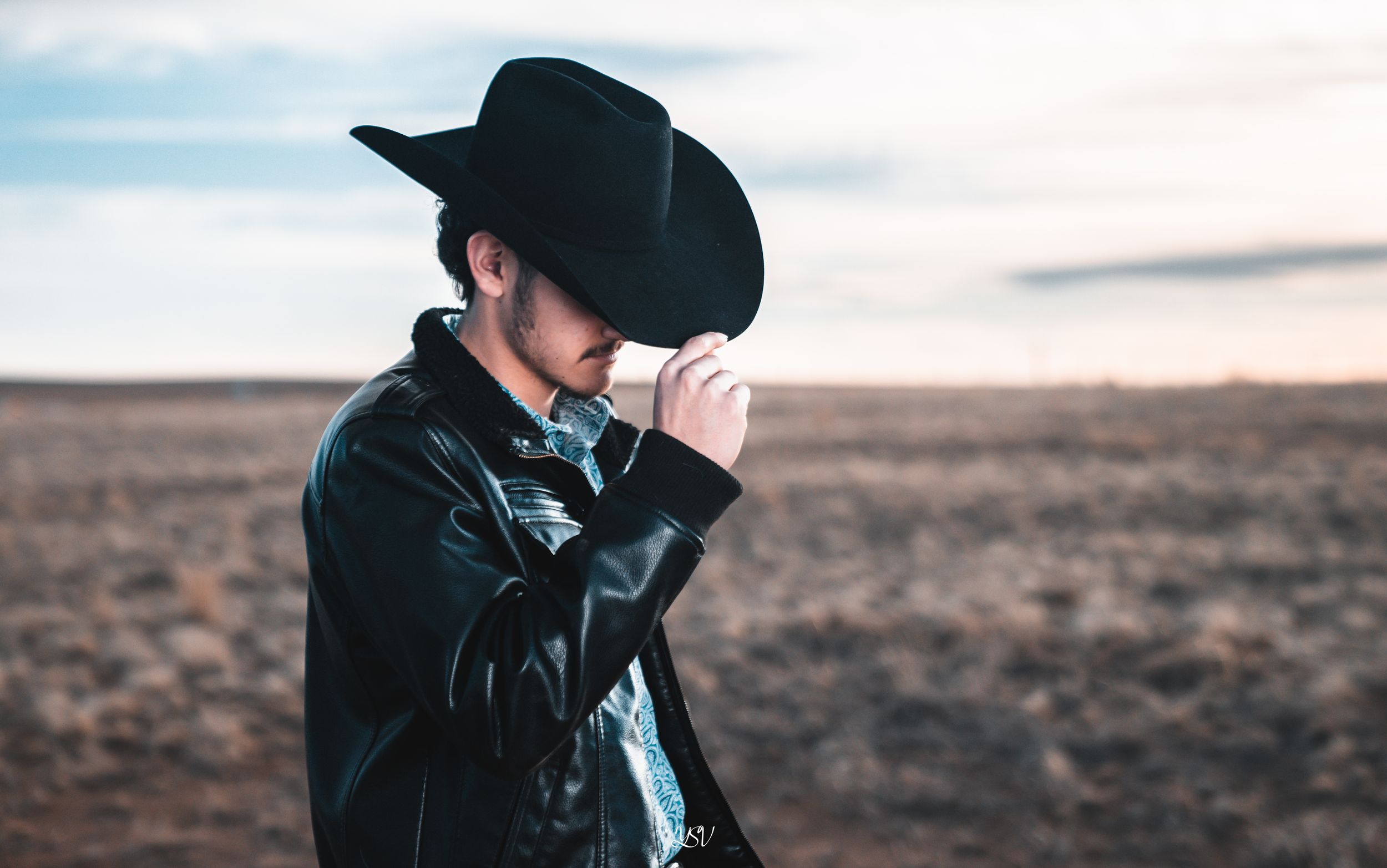 A person in dark clothing stands in silhouette against a moody desert landscape at sunset.