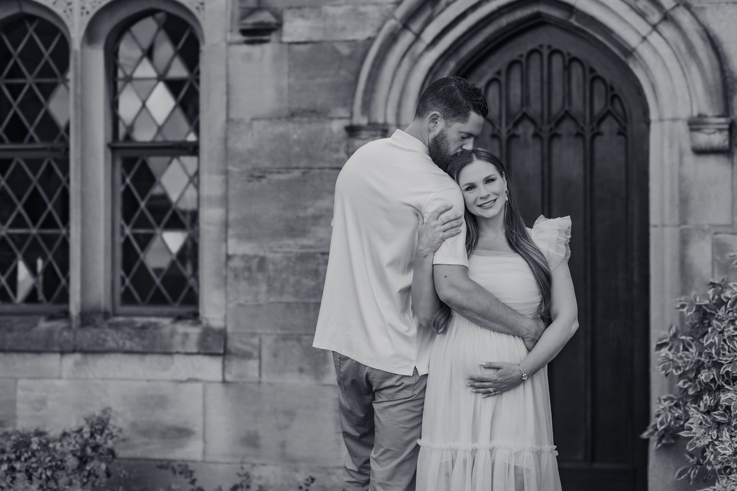 An expecting couple share an embrace as she cradles her baby bump