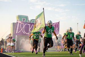 Football players run across a field during practice with colorful graffiti walls in the background.