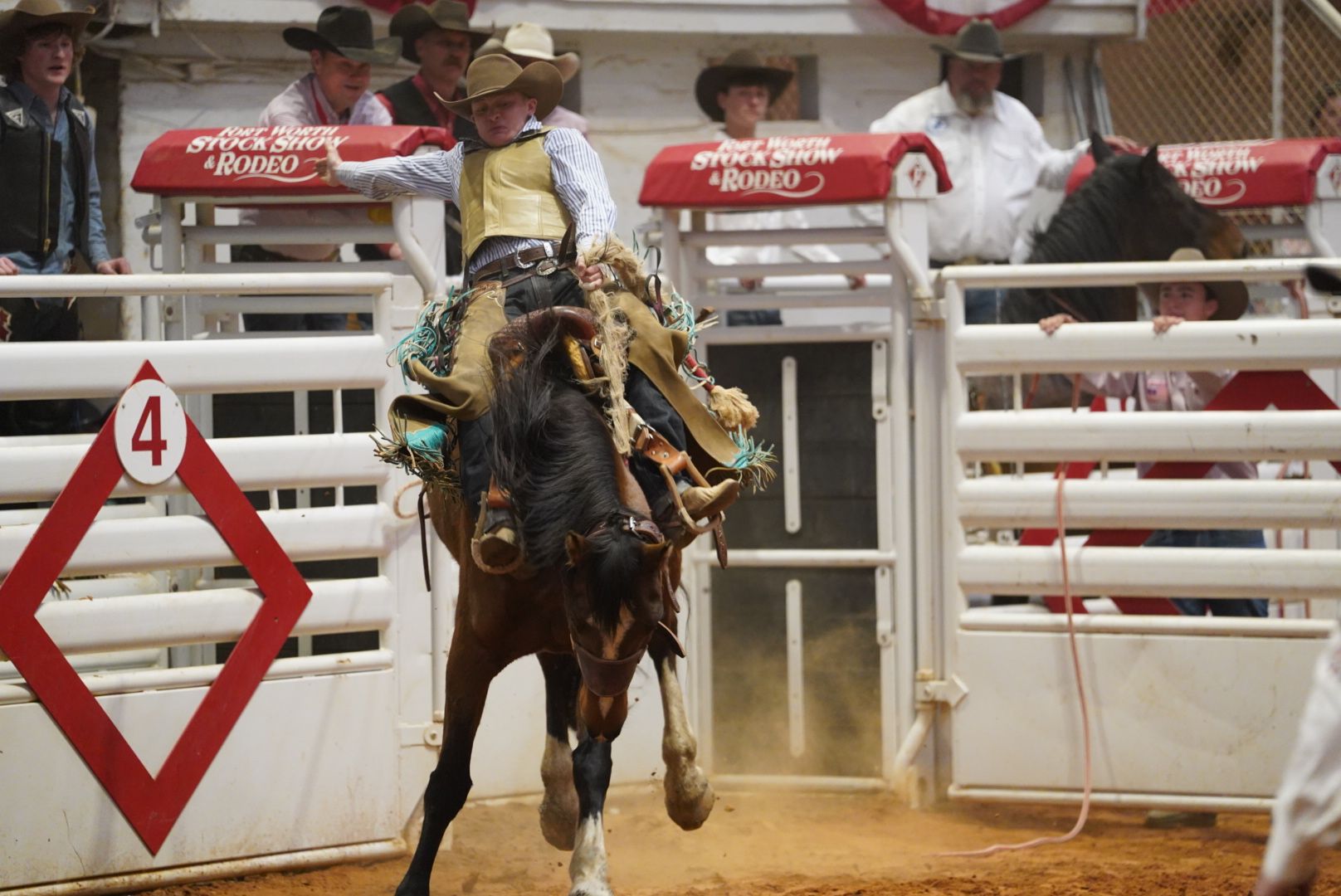 Rodeo competitors racing through barrel course in indoor arena.