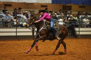 Horse and rider performing barrel racing pattern at indoor rodeo event.