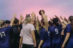 Sports fans in navy blue jerseys cheer and raise their arms in celebration at a game.