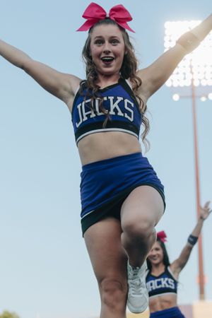 Cheerleaders in navy uniforms perform high kicks with pink bows in their hair.
