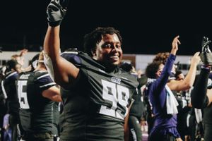 Football players in dark uniforms celebrate on the sidelines during a night game.