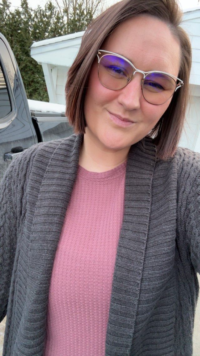 Portrait of photographer Hannah smiling outdoors, wearing glasses, a pink sweater, and gray cardigan.