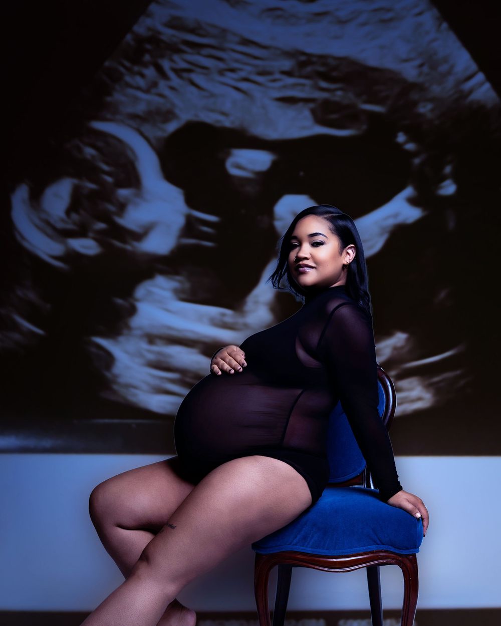 Figure sitting on a wooden chair against dark background with dramatic blue lighting and abstract swirling patterns projected behind.