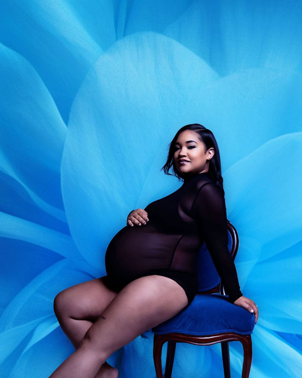 Artistic fashion photo with dramatic blue floral background featuring someone posing confidently on a blue chair.