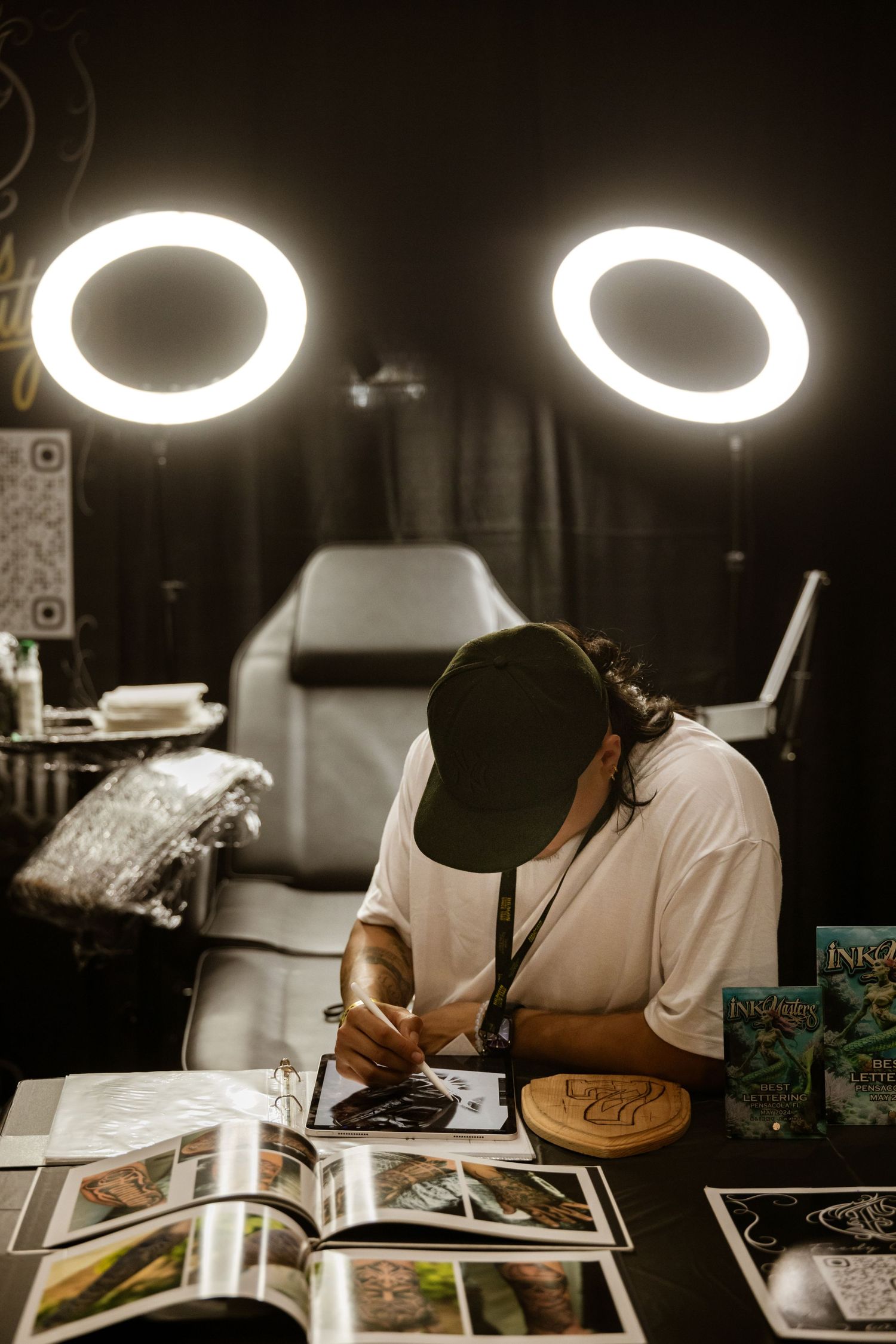 Professional tattoo workspace with ring lights and reference materials on the table.