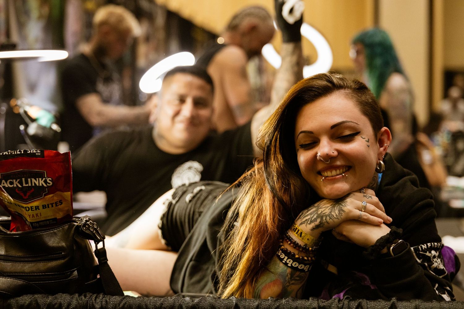 Person lying down getting tattooed at a busy convention or event.