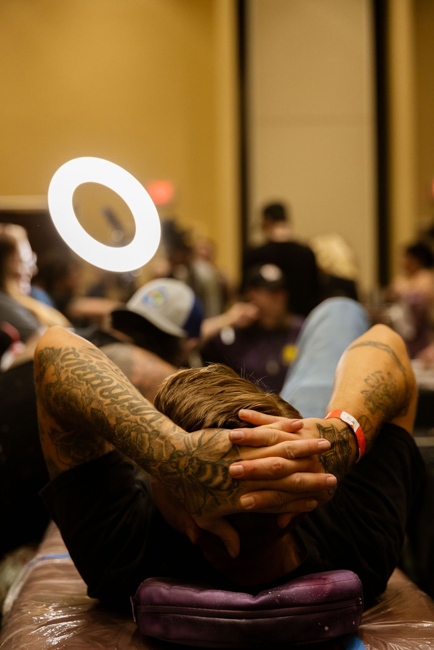 Tattooed hands resting beneath a ring light at a tattoo event.